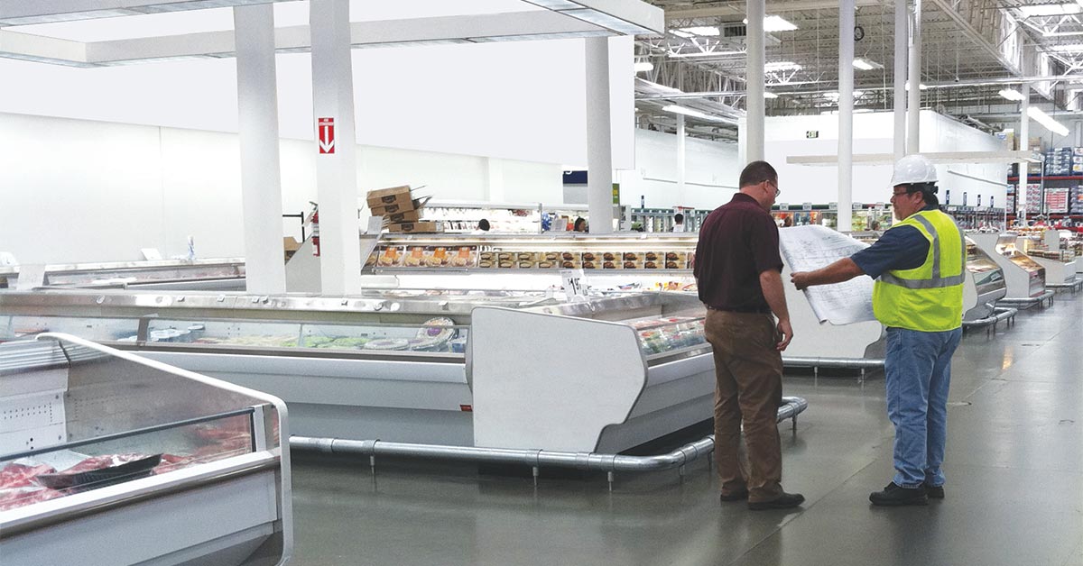 Two men standing in a supermarket discussing plans to remodel