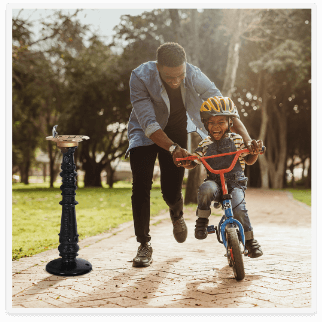 Classic outdoor drinking fountain with a father teaching his son to ride a bike